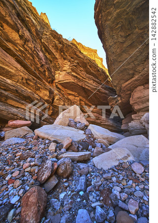Towering Slot Canyon Walls and Rocky Floor Under Clear Blue Sky 142882542