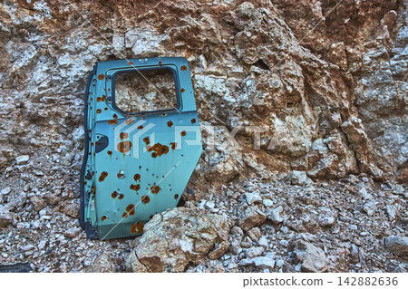 Abandoned Car Door with Bullet Holes Against Rocky Desert Cliff in Nevada Abandoned Car Door with Bullet Holes Against Rocky Desert Cliff in Nevada 142882636
