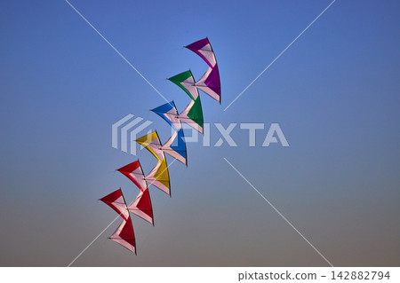 Colorful Kites Flying in Formation at Kite Festival Under Clear Blue Sky Colorful Kites Flying in Formation at Kite Festival Under Clear Blue Sky 142882794