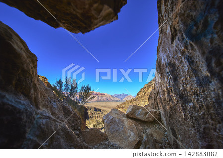Cave Entrance Framing Desert Landscape with Rocky Walls and Distant Nevada Mountains Cave Entrance Framing Desert Landscape with Rocky Walls and Distant Nevada Mountains 142883082