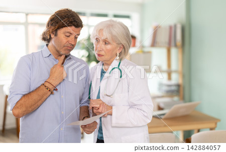 Elderly doctor discussing medical tests with sad man in medical office Elderly doctor discussing medical tests with sad man in medical office 142884057