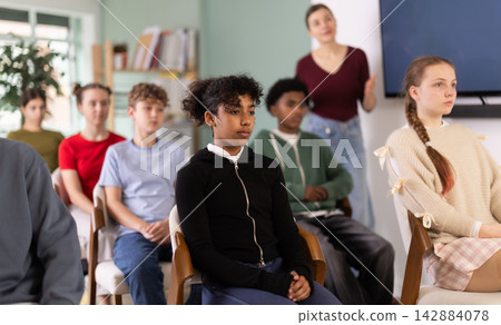Teenage students listening to lecture while teacher stands in background 142884078