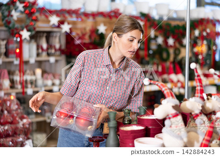 Woman selecting christmas decorations in salesroom of decorative goods shop Woman selecting christmas decorations in salesroom of decorative goods shop 142884243