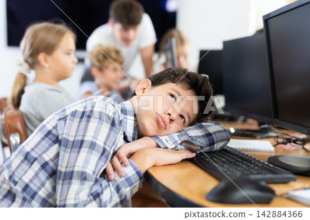 Tired preteen boy sleeping at computer table in training room 142884366