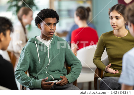 African American boy sits in a circle of teenagers at a lecture, they do a practical lesson African American boy sits in a circle of teenagers at a lecture, they do a practical lesson 142884384