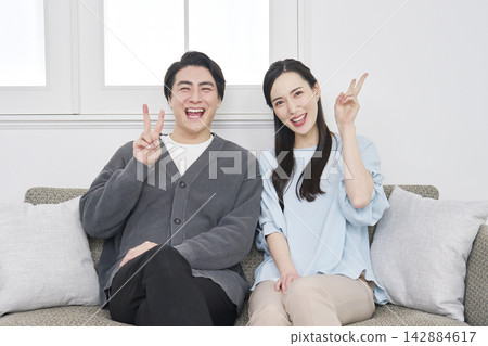 Middle-aged couple in their living room, making a peace sign. Middle-aged couple in their living room, making a peace sign. 142884617