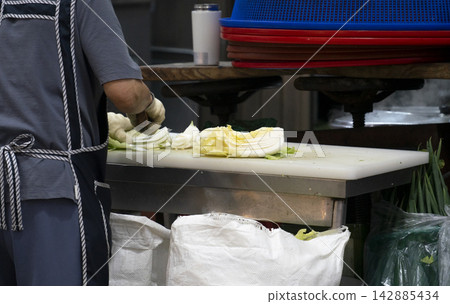 Vendor chopping fresh napa cabbage on a large cutting board at a local market Vendor chopping fresh napa cabbage on a large cutting board at a local market 142885434