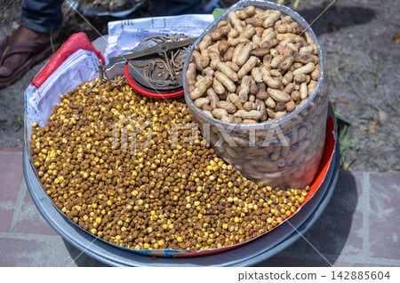 Street vendor tray displaying roasted chickpeas and peanuts in plastic bag with weighing scale. Popular South Asian crunchy snack food for outdoor leisure time. Street vendor tray displaying roasted chickpeas and peanuts in plastic bag with weighing scale. Popular South Asian crunchy snack food for outdoor leisure time. 142885604