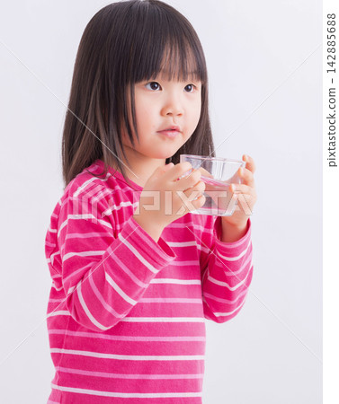 Cute little girl holding a glass and drinking fresh water against a white background. Cute little girl holding a glass and drinking fresh water against a white background. 142885688