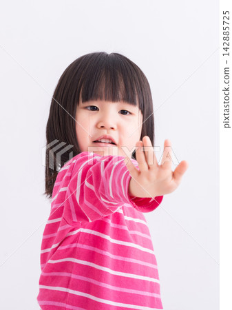 Serious little Asian girl extending her open hand in a stop gesture. Serious little Asian girl extending her open hand in a stop gesture. 142885725