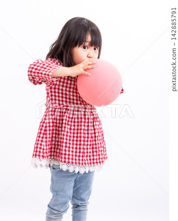 Cute little Asian girl in a red plaid shirt blowing up a pink balloon, standing against a white background, childhood fun and party preparation concept. Cute little Asian girl in a red plaid shirt blowing up a pink balloon, standing against a white background, childhood fun and party preparation concept. 142885791