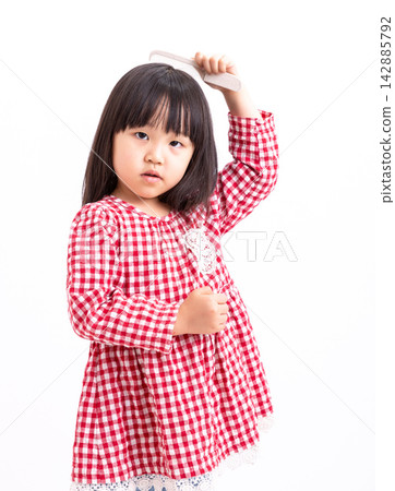 Adorable young Asian girl holding a comb and brushing her neat black hair, looking at camera on white background, daily hygiene and morning routine concept. Adorable young Asian girl holding a comb and brushing her neat black hair, looking at camera on white background, daily hygiene and morning routine concept. 142885792