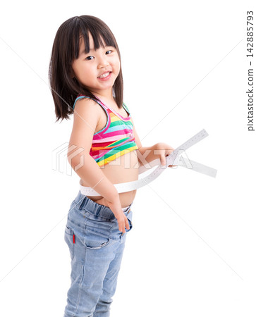 Happy little Asian girl measuring her waist with a white tape measure, standing against a white studio background, fitness, health and growing up concept. Happy little Asian girl measuring her waist with a white tape measure, standing against a white studio background, fitness, health and growing up concept. 142885793