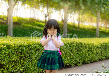Sad Asian Little Schoolgirl Holding Face with Hands in Park Sad Asian Little Schoolgirl Holding Face with Hands in Park 142885797