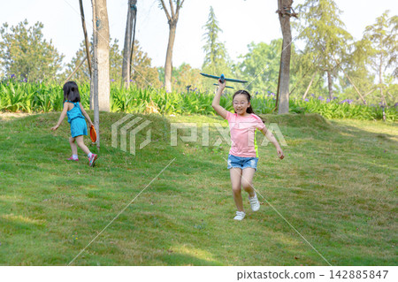 Energetic Asian girl running on a grassy slope and throwing a blue toy airplane into the air, aspiring to fly and childhood dream concept. 142885847