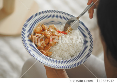 Eating a plate of rice with chicken and sauce in a casual setting Eating a plate of rice with chicken and sauce in a casual setting 142885952