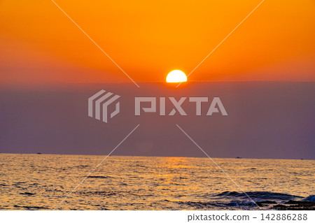 絢麗的橙色夕陽灑在海面上,緩緩沉入一層薄薄的雲層之後。 絢麗的橙色夕陽灑在海面上,緩緩沉入一層薄薄的雲層之後。 142886288