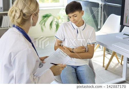 Pediatrician consulting teen boy with abdominal pain during exam in clinic Pediatrician consulting teen boy with abdominal pain during exam in clinic 142887170