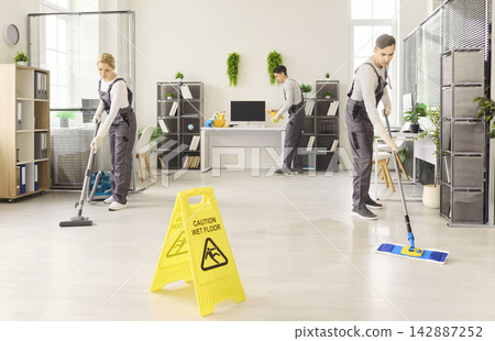 Cleaning crew mopping and vacuuming modern office with caution wet floor sign Cleaning crew mopping and vacuuming modern office with caution wet floor sign 142887252