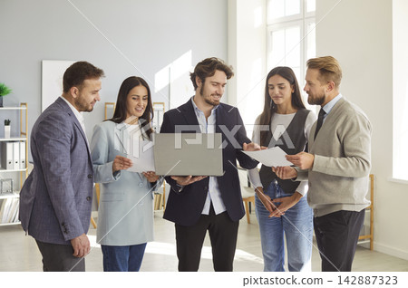 Businessman at laptop and people group, team leader showing new project online at company meeting Businessman at laptop and people group, team leader showing new project online at company meeting 142887323