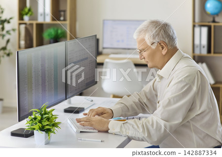 Senior analyst typing financial data on keyboard at dual monitors in office Senior analyst typing financial data on keyboard at dual monitors in office 142887334