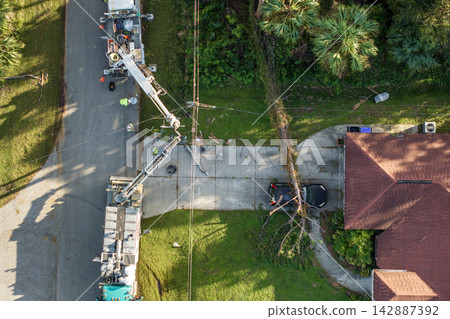 Electrician workers repairing damaged power lines using bucket trucks after hurricane in Florida residential area Electrician workers repairing damaged power lines using bucket trucks after hurricane in Florida residential area 142887392