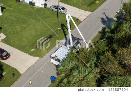 Aerial view of electrician utility worker trimming tree branches around power lines in Florida suburban area 142887394
