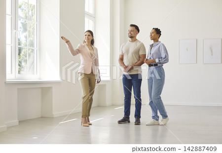 Real estate agent giving a property tour to young couple in empty apartment Real estate agent giving a property tour to young couple in empty apartment 142887409
