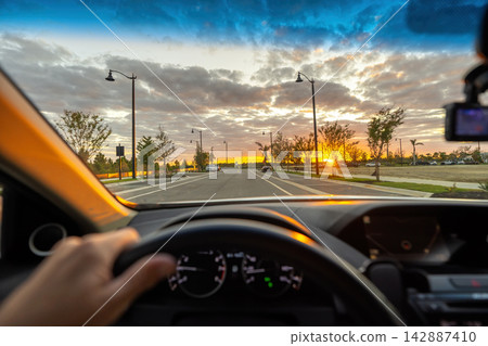 Driver point of view on Florida city street at sunset with hands on steering wheel and traffic flowing through busy urban neighborhood. Driver point of view on Florida city street at sunset with hands on steering wheel and traffic flowing through busy urban neighborhood. 142887410