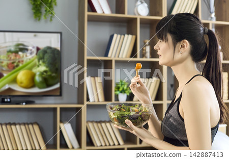 Active woman enjoying healthy salad while viewing TV recipe program at home Active woman enjoying healthy salad while viewing TV recipe program at home 142887413