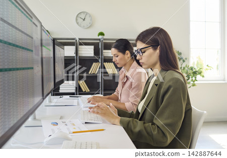 Women analysts working at computers, monitoring data and reports in office Women analysts working at computers, monitoring data and reports in office 142887644