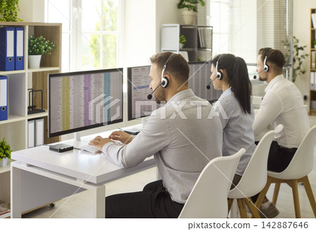 Call center agents with headsets working at computers in modern open office 142887646