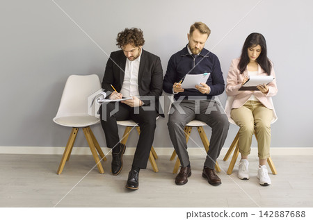 Job interview candidates filling forms while waiting in office chairs for hiring 142887688