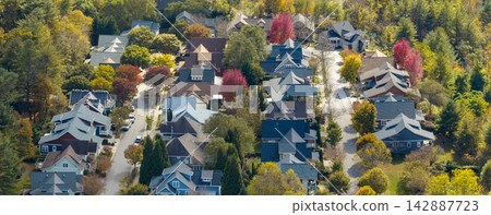 Residential homes overlooking colorful forested hills during peak fall season. Peaceful mountain landscape filled with brilliant autumn foliage. Residential homes overlooking colorful forested hills during peak fall season. Peaceful mountain landscape filled with brilliant autumn foliage. 142887723