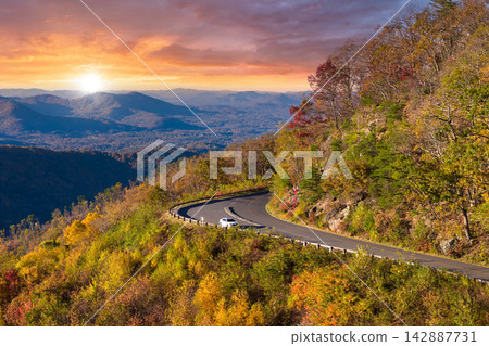 Vehicle parked at quiet viewpoint overlooking vibrant fall foliage. Peaceful landscape with colorful trees stretching in distance. Vehicle parked at quiet viewpoint overlooking vibrant fall foliage. Peaceful landscape with colorful trees stretching in distance. 142887731