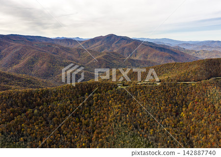 Scenic empty road in North Carolina mountains lined with brilliant autumn trees. Colorful forest creates a peaceful fall travel destination. Scenic empty road in North Carolina mountains lined with brilliant autumn trees. Colorful forest creates a peaceful fall travel destination. 142887740