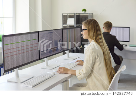 Businesswoman analyzing financial data on multi monitors in modern office Businesswoman analyzing financial data on multi monitors in modern office 142887743