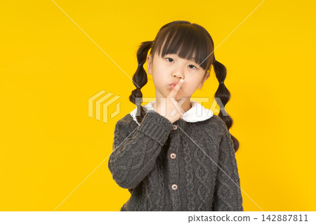 Cute little girl holding a finger to her lips for a silence gesture on a yellow background. Cute little girl holding a finger to her lips for a silence gesture on a yellow background. 142887811