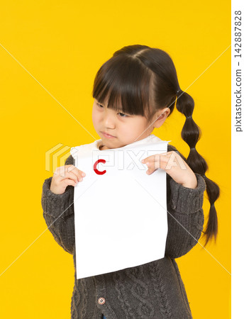 Little schoolgirl looking at her test paper with a bad grade C and feeling sad. Little schoolgirl looking at her test paper with a bad grade C and feeling sad. 142887828