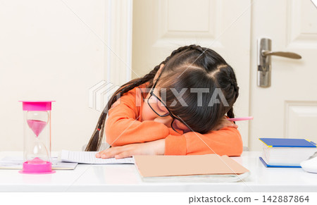 Tired schoolgirl resting her head on her arms and sleeping over her school books. Tired schoolgirl resting her head on her arms and sleeping over her school books. 142887864