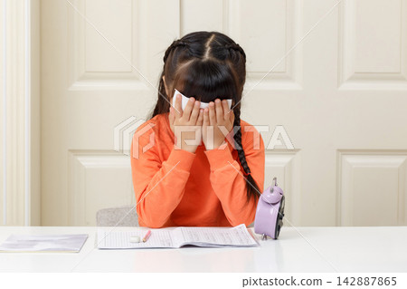 Sad little girl covering her face with hands and crying over her desk with a clock nearby. Sad little girl covering her face with hands and crying over her desk with a clock nearby. 142887865