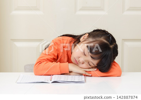 Tired schoolgirl resting her head on her arms and sleeping over her school books. Tired schoolgirl resting her head on her arms and sleeping over her school books. 142887874