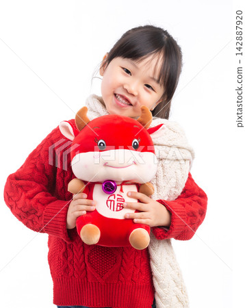 Smiling little girl hugging a red ox plush toy, celebrating the Year of the Ox, Chinese New Year theme.The Chinese character embroidered above: "Fu" (Good Fortune) 142887920