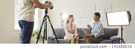 Professional female journalist interviewing woman sitting on sofa in studio recording video Professional female journalist interviewing woman sitting on sofa in studio recording video 142888038