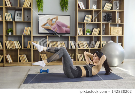 Woman training abs home with online TV workout, bicycle crunches cardio exercise 142888202