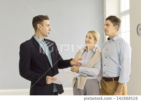 Real estate agent advising couple during property tour in spacious light apartment Real estate agent advising couple during property tour in spacious light apartment 142888528