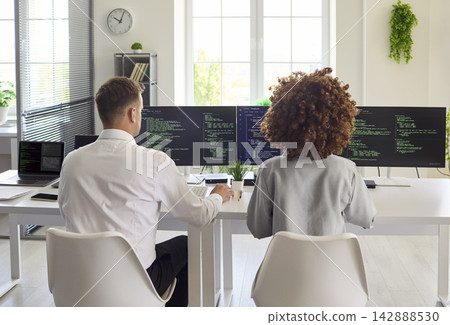 Developers pair programming at multi monitor workstation in modern bright office 142888530