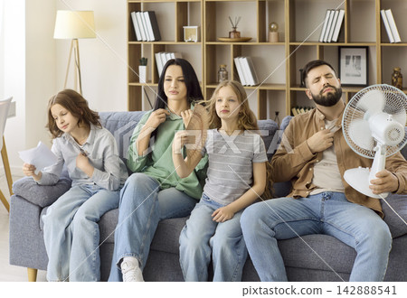 Overheated family at home using a fan during summer heat, parents and children Overheated family at home using a fan during summer heat, parents and children 142888541