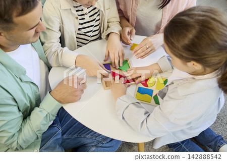 Parents and kids assembling geometric shapes puzzle game together at home 142888542