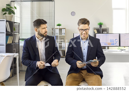 Two office employees compare salaries, one unhappy as colleague counts more cash Two office employees compare salaries, one unhappy as colleague counts more cash 142888552